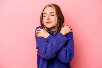 Young caucasian woman isolated on pink background hugs, smiling carefree and happy.