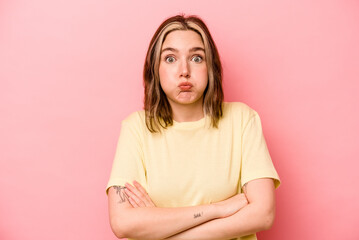 Young caucasian woman isolated on pink background blows cheeks, has tired expression. Facial...