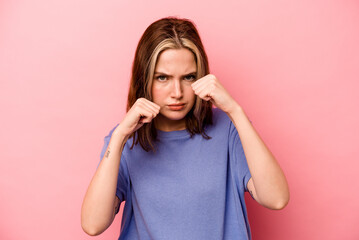 Young caucasian woman isolated on pink background throwing a punch, anger, fighting due to an...