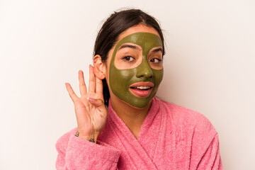 Young hispanic woman wearing a facial mask isolated on white background trying to listening a gossip.