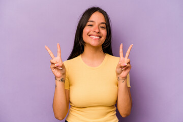 Young hispanic woman isolated on purple background showing victory sign and smiling broadly.
