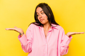 Young hispanic woman isolated on yellow background confused and doubtful shrugging shoulders to hold a copy space.
