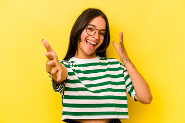 Young hispanic woman isolated on yellow background feels confident giving a hug to the camera.