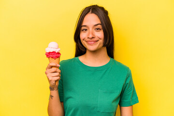 Young hispanic woman eating an ice cream isolated on yellow background