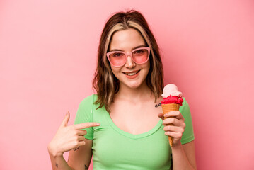 Young caucasian woman holding an ice cream isolated on pink background person pointing by hand to a shirt copy space, proud and confident