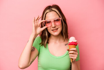 Young caucasian woman holding an ice cream isolated on pink background excited keeping ok gesture on eye.