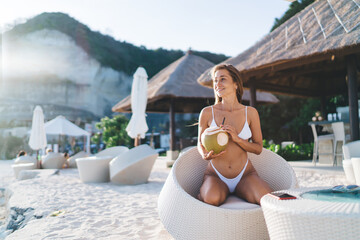 Caucasian girl with coconut fruit enjoying summertime vibes during vacations at Maldives, charming...