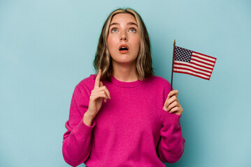 Young caucasian woman holding a American flag isolated on blue background pointing upside with opened mouth.