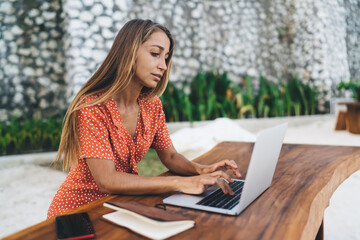 Millennial female freelancer browsing web information on laptop computer working remotely outdoors, skilled copywriter searching text publication on netbook technology using wireless connection
