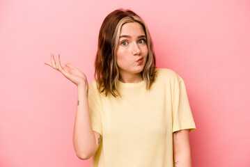 Young caucasian woman isolated on pink background doubting and shrugging shoulders in questioning...