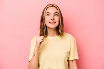 Young caucasian woman isolated on pink background indicates with both fore fingers up showing a...