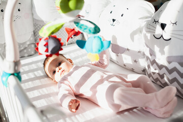 Beautiful baby wearing pink sleepsuit playing under to toy of hanging mobile.