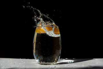tangerine wedge entering and splashing into a glass of water, fruit, citrus, black background, concept of vitality, health, well-being, vitamin