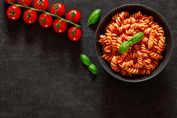Fusilli, cooked pasta with tomato sauce, tomatoes cherry and basil leaf, on dark background, top...