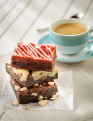 Pile of three brownies on a wood table, with a coffee cup on the background
