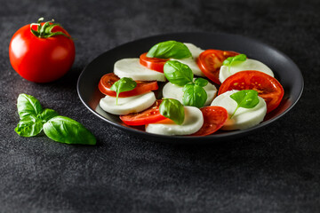 Caprese, Italian antipasto, mozzarella, tomato and basil on dark background, side view, selective focus.