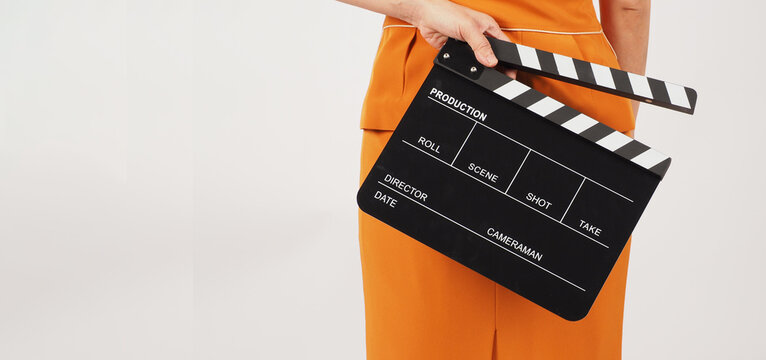 Woman hold clapper board and turn around.She wear a yellow suit on white background.Body part