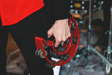 Female musician playing tambourine and singing into the microphone, with the musical band performing on stage in the background during jazz rock concert