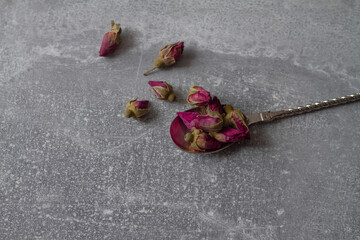 Dried pink rose buds on a spoon on a gray background