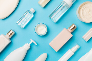 Different cosmetic bottles and container on color background, top view