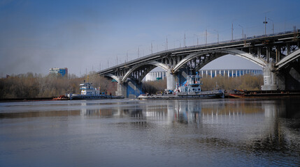 Two tugs pushing barges diverge under different spans of the bridge. River navigation with barges...