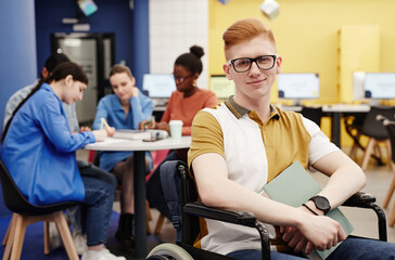 Vibrant portrait of red haired young man with disability in college library looking at camera, copy...