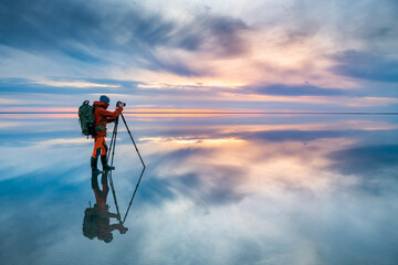 Photographer traveler taking photo of the salt lake at sunset. Blue sky with clouds are reflected...