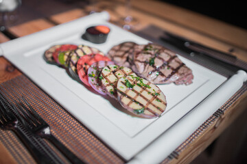 A plate of grilled beef meat with grilled slices of potatoes, tomatoes and onions