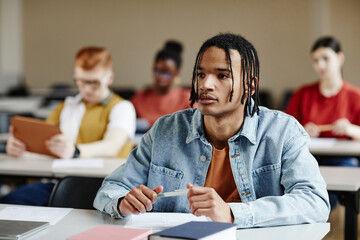 Portrait of black teenage boy with braids listening to lecture in school or college, copy space