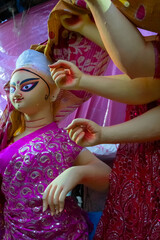 Kolkata, West Bengal, India - 7th October 2018: Clay idol of Goddess Saraswati and hands of Durga, covered under Sari - traditional Indian dress for preparation of 