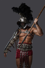 Shot of ancient roman fighter with plumed helmet throwing spear against grey background.