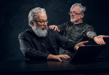 Shot of two modern senior men with gray hairs using laptop discussing some plans.