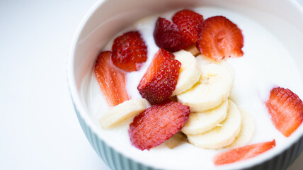 Close up white natural greek yogurt cream with fresh juicy strawberry and sliced banana in round bowl on white background. Top view. Healthy breakfast from nutritionist, good for digestion.