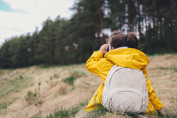 Little explorer, girl with binoculars plays in the forest. Search and research. Travel and adventure concept. Kids club, camping