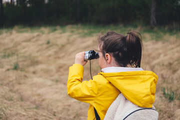 Little explorer, girl with binoculars plays in the forest. Search and research. Travel and adventure concept. Kids club, camping