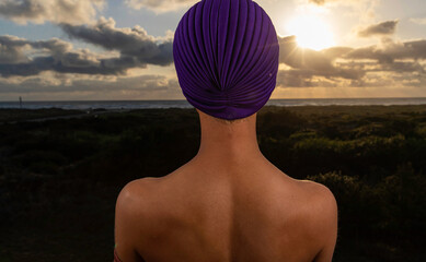 African American woman outside with ocean beach view wearing purple turban
