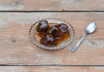 Close-up of preserved whole ripe fig in a dish with a spoon on wooden surface. Ripe figs syrup jam over plate. Traditional Mediterranean confiture. Sweet food. Front view.