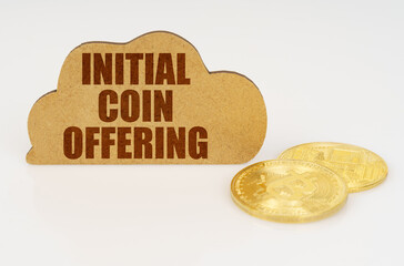 Bitcoins lie on a white surface and there is a sign - a cloud with the inscription - Initial coin...