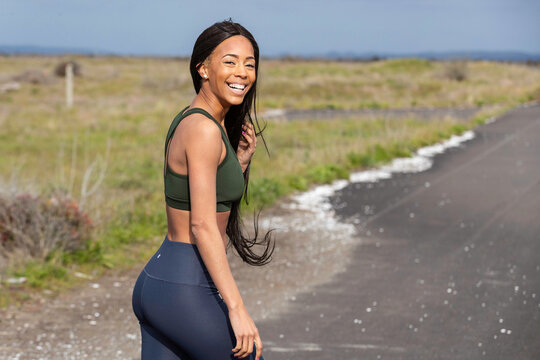 African American woman with long black hair exercising outside on country road.