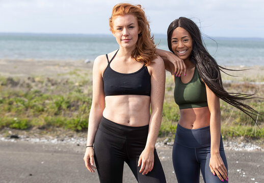 Two woment together at ocean beach wearing exercise clothes.
