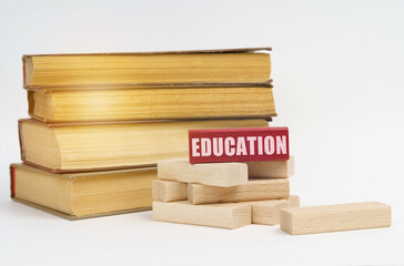 On a white surface, a stack of books and wooden blocks, on a red block there is an inscription - education
