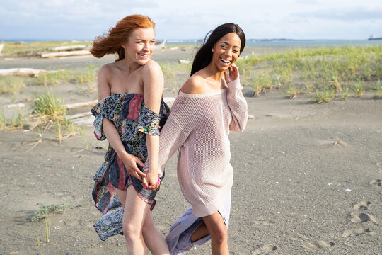 African American woman with long black hair and Caucasin woman with red hair and freckles outside at ocean beach.