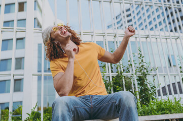 Bottom viev young cool fun cheerful man 20s wear yellow t-shirt sitting listen to music in...