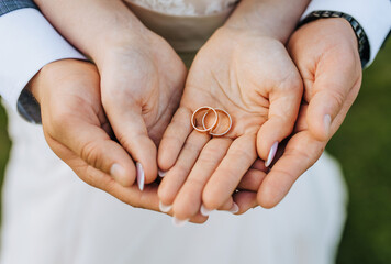 The bride and groom hold round gold rings in their hands, close-up on the palms. Wedding portrait of newlyweds, photography, concept.