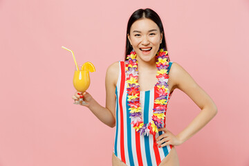 Happy fun young woman of Asian ethnicity in striped one-piece swimsuit hawaii lei hold orange...