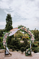 A round wedding arch decorated with colorful flowers and fabric stands in a park, a garden in...