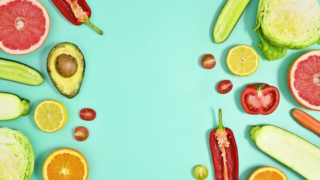 Sliced pieces of fresh organic fruits and vegetables makes creative copy space on cyan background. Food concept. Stop motion flat lay