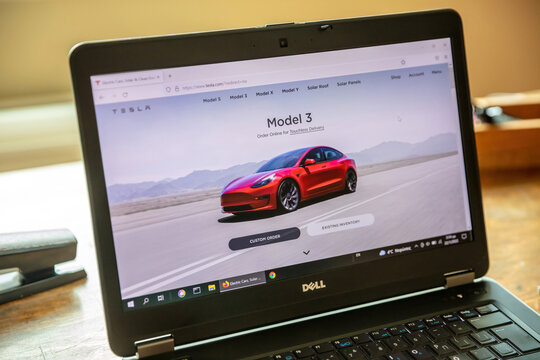 TESLA CAR SELECTION. Ad, online red Tesla model 3 electric auto. Computer laptop on table, close up