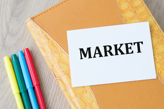 Market inscription on a white card on a yellow background on a wooden table next to colored markers