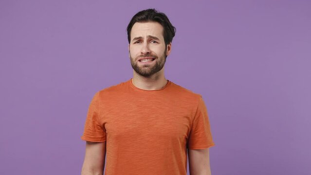 Fun confused shy shamed young brunet bearded man 20s wears red t-shirt look camera spreading hands say oops ouch oh omg i am so sorry isolated on plain pastel light purple background studio portrait
